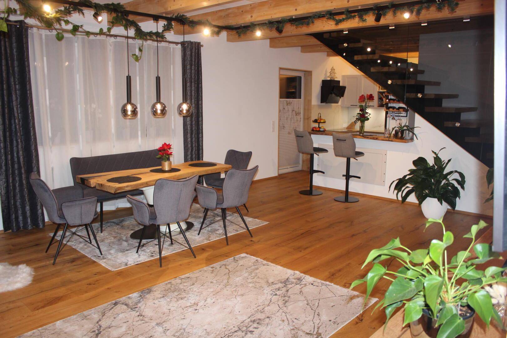 Geräumiger Essbereich mit Holzboden und moderner Küche im Hintergrund, verbunden durch eine Bar.