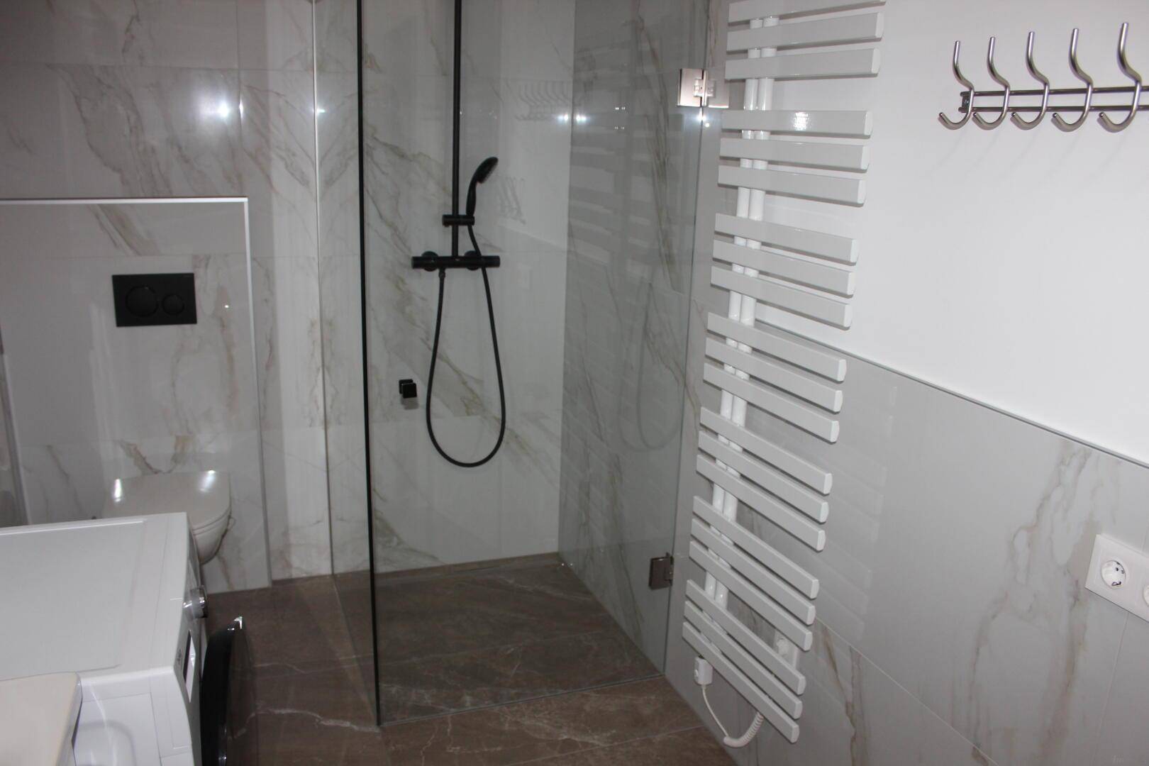 Elegantes Badezimmer mit begehbarer Dusche, Wand-WC und modernem Handtuchheizkörper.