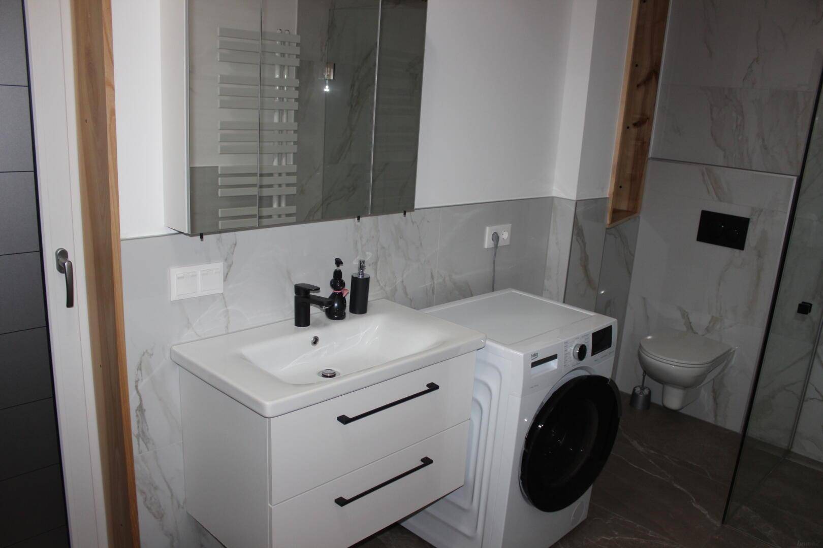 Helles Badezimmer mit modernem Waschtisch, Spiegelschrank und integrierter Waschmaschine.