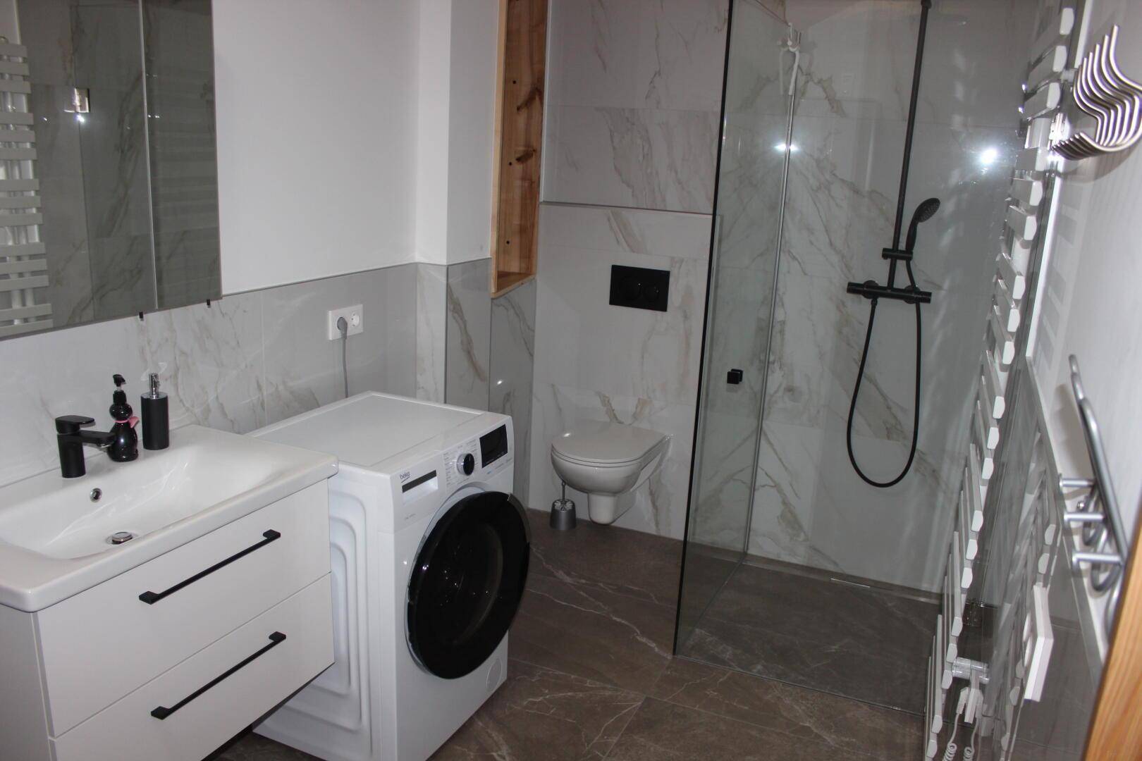 Modernes Badezimmer mit begehbarer Dusche, Waschmaschine und eleganten Marmorfliesen.