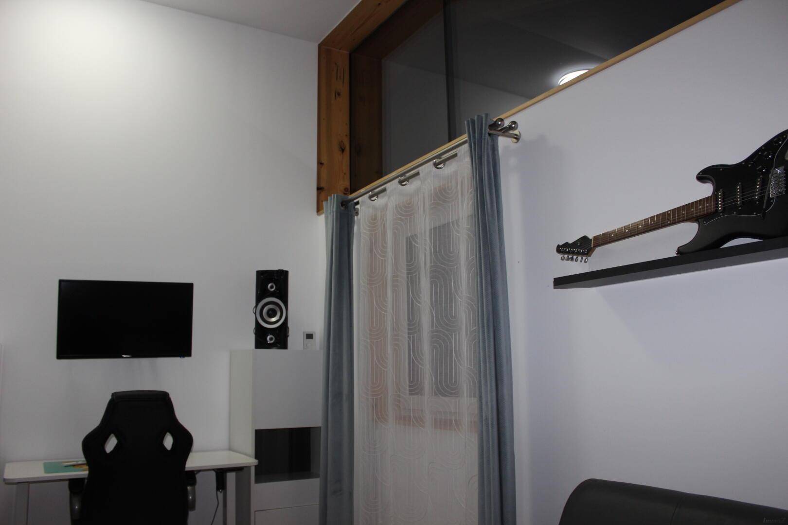 Modernes Zimmer mit Schreibtisch, Fernseher und Gitarre, ideal als Arbeits- oder Hobbyraum.