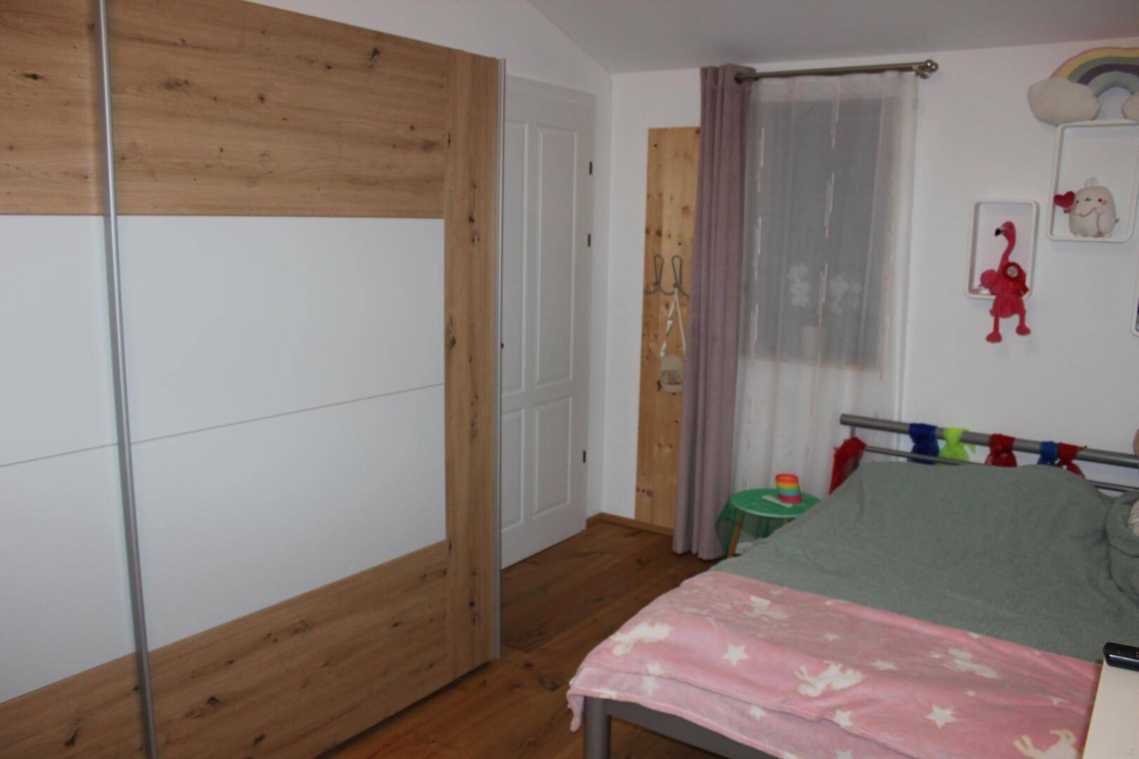 Helles Kinderzimmer mit Bett, großem Schrank und Holzboden, ideal für junge Bewohner.