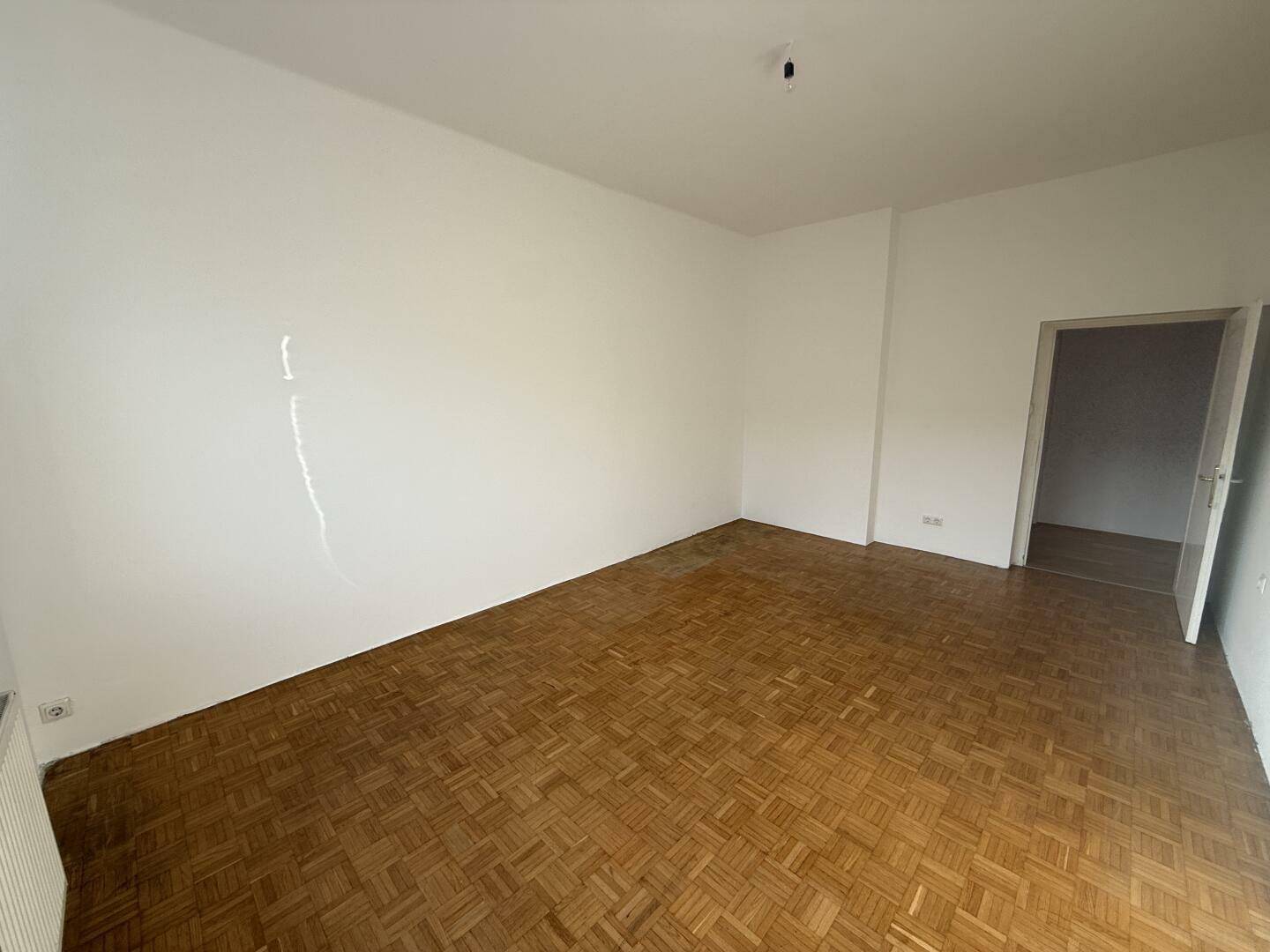 Helles Zimmer mit Parkettboden und Zugang zu einem weiteren Raum, ideal für flexible Nutzung.