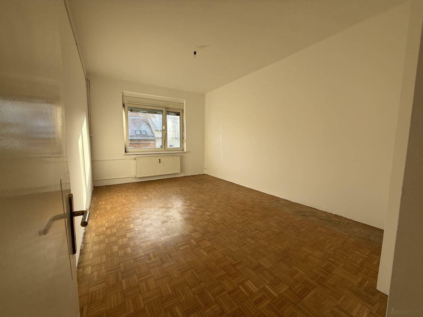 Geräumiges Zimmer mit Parkettboden und Fenster, das viel Tageslicht bietet.