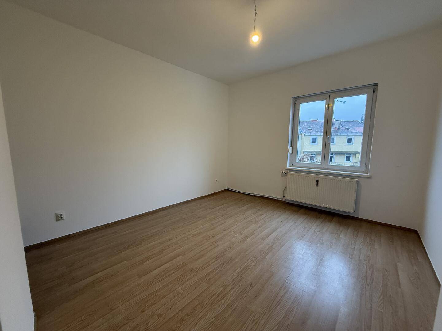 Helles, leeres Zimmer mit Laminatboden und Fenster, bereit zur individuellen Gestaltung.