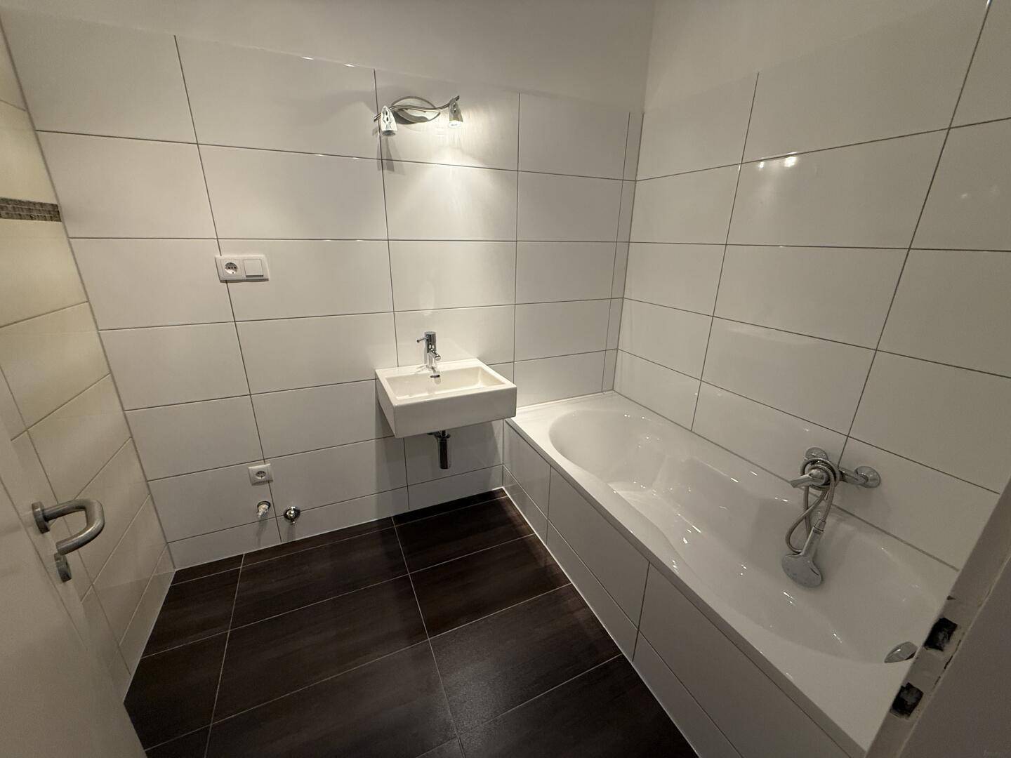 Modern gefliestes Badezimmer mit Badewanne und wandmontiertem Waschbecken.