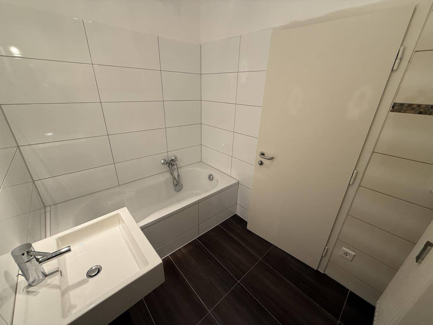 Helles Badezimmer mit Badewanne und modernem Waschbecken, komplett gefliest.