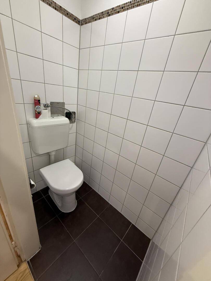 Kleines, funktionales WC mit weißen Fliesen und dunklem Boden, sauber und gepflegt.