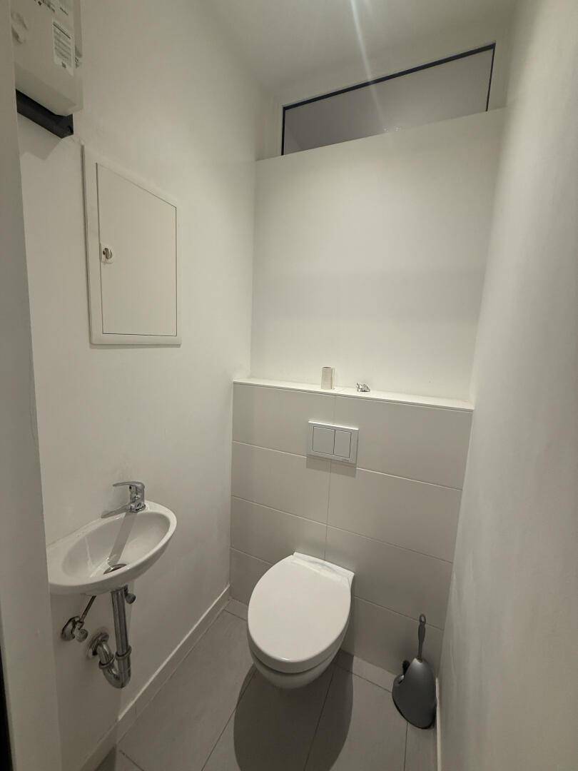 Modernes Gäste-WC mit wandhängendem WC, kleinem Waschbecken und hellen Fliesen.