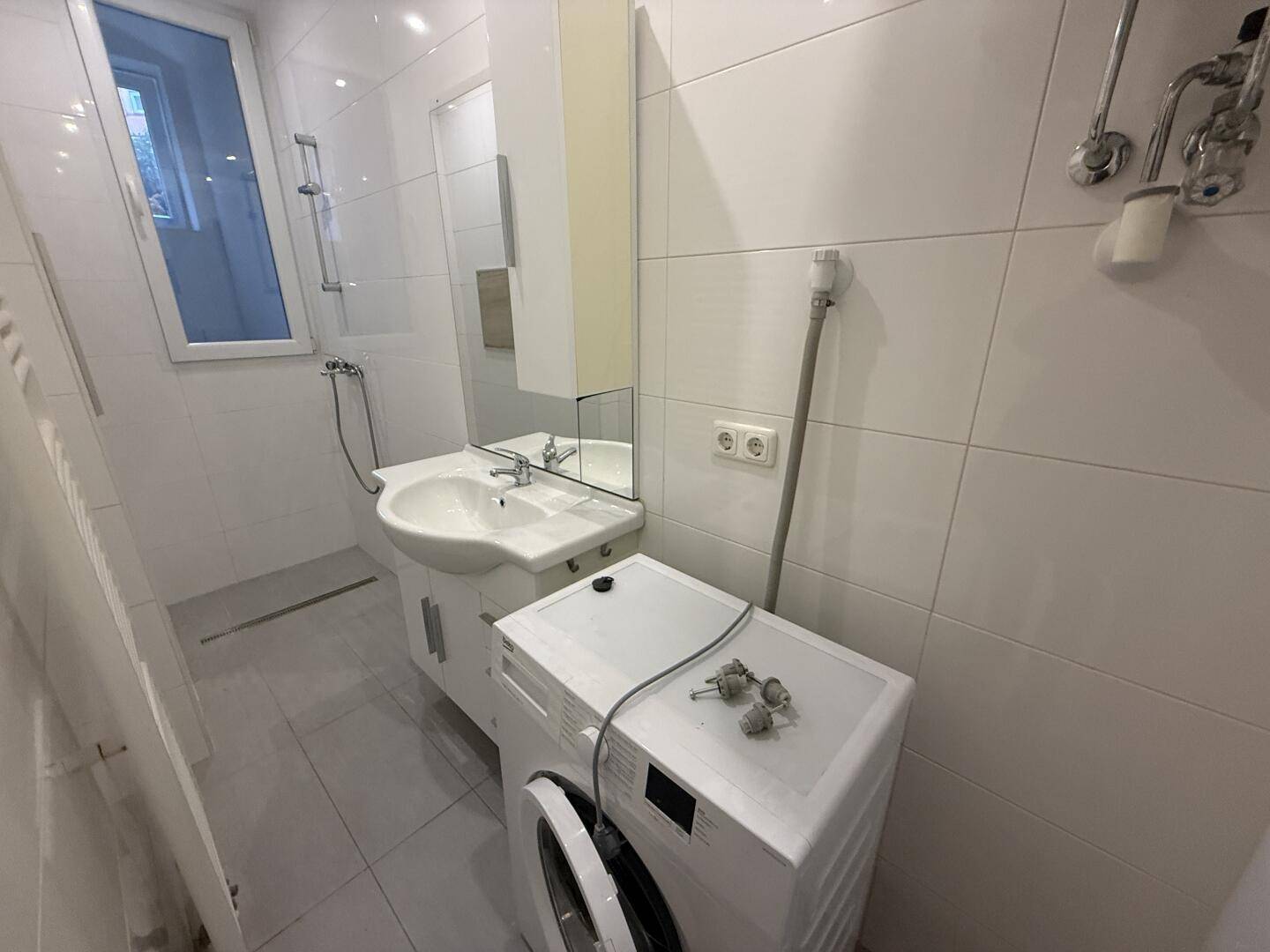 Modernes Badezimmer mit Waschbecken, Spiegelschrank und integrierter Waschmaschine.