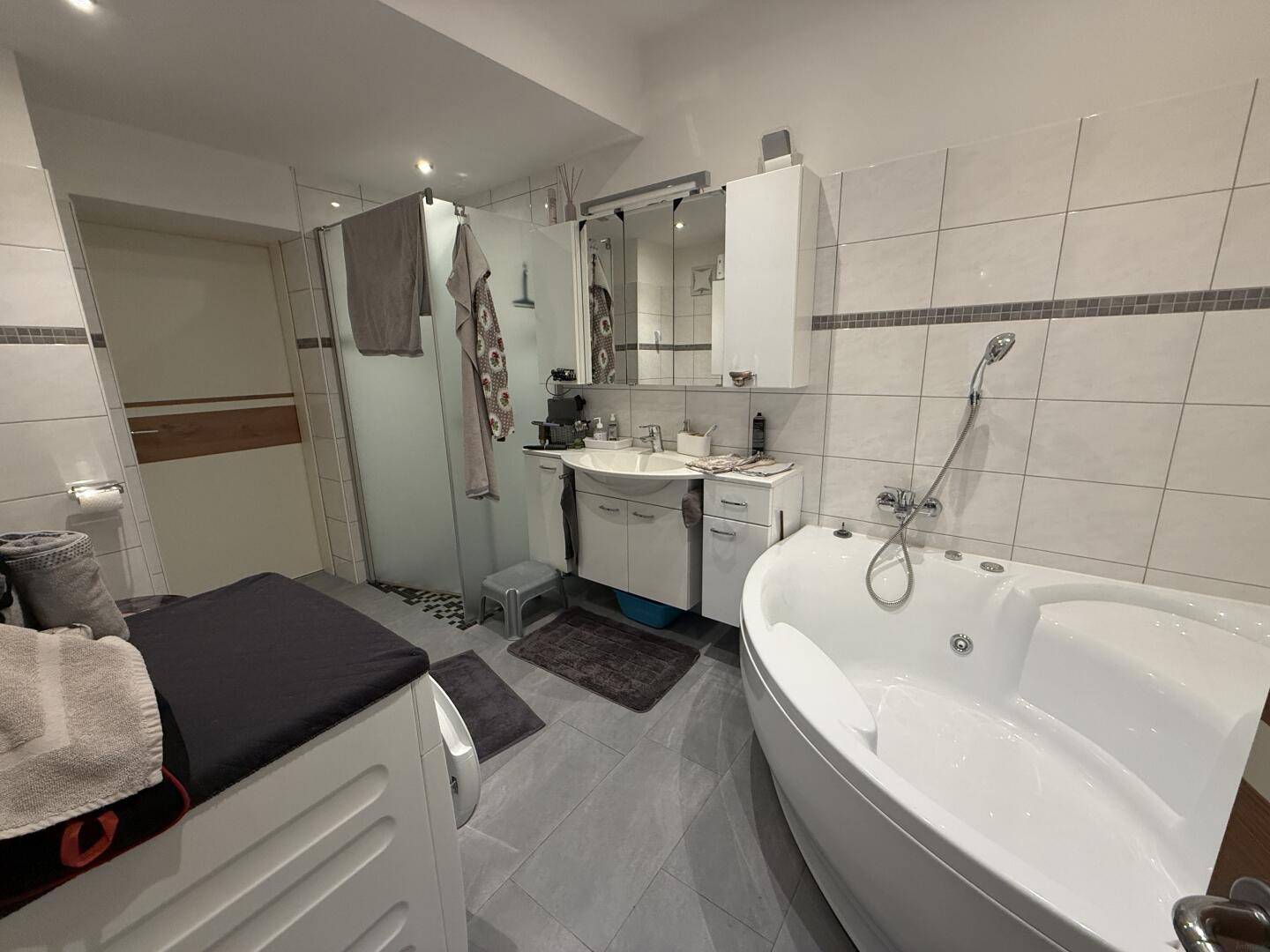 Helles Badezimmer mit Eckbadewanne, Duschkabine, Waschbecken und Fliesenboden.