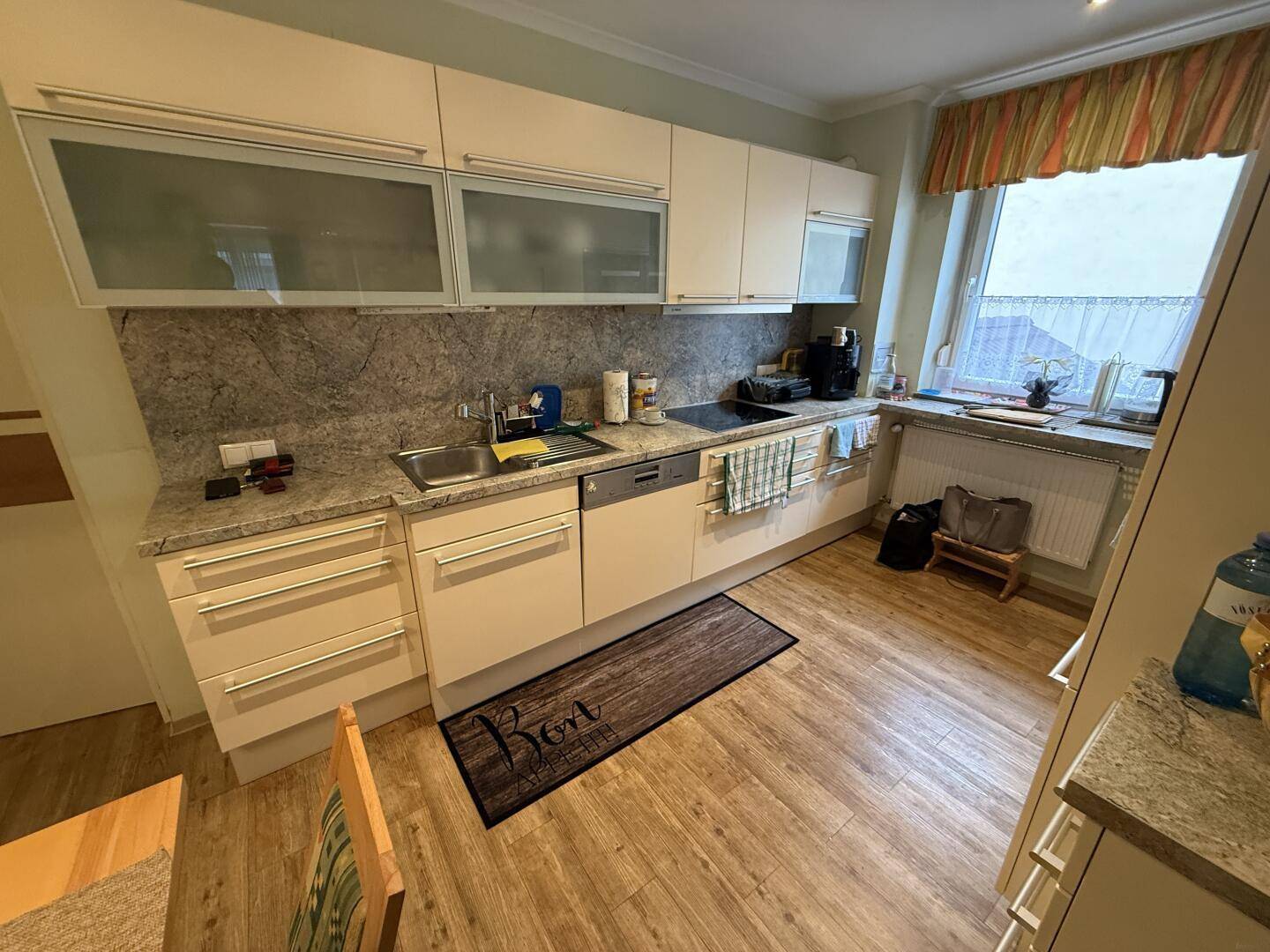 Helle Einbauküche mit cremefarbenen Schränken, Granitarbeitsplatten und Fenster mit Vorhängen.