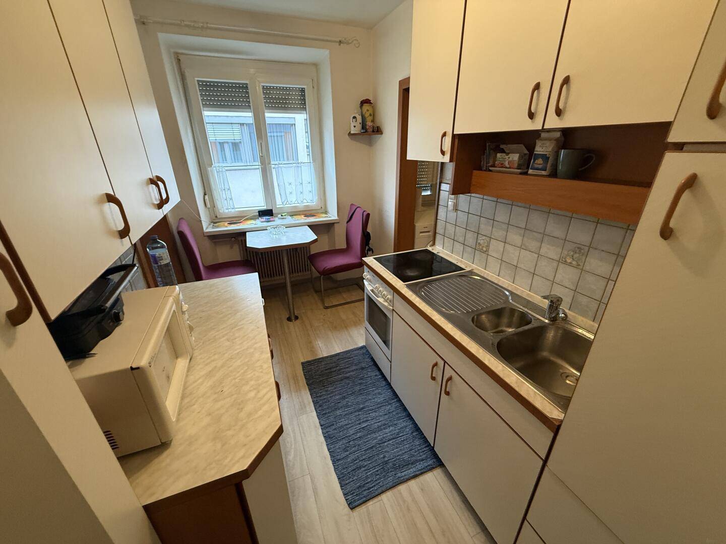 Kleine Küche mit weißen Schränken, kompakter Kochzeile und Essbereich am Fenster.