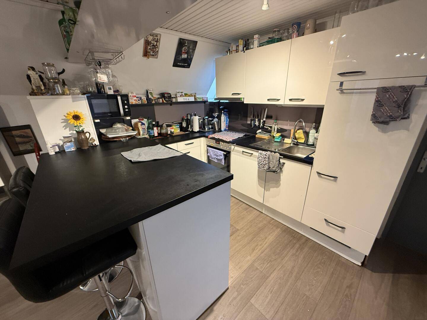 Moderne Küche mit weißen Hochglanzschränken, dunklen Arbeitsplatten und Kücheninsel unter Dachschräge.