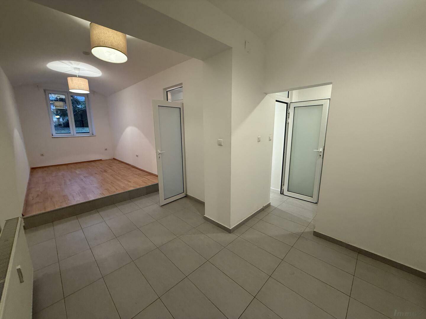 Geräumiger Bereich mit Fliesenboden und Zugang zu einem erhöhten Wohnraum mit Fenster.