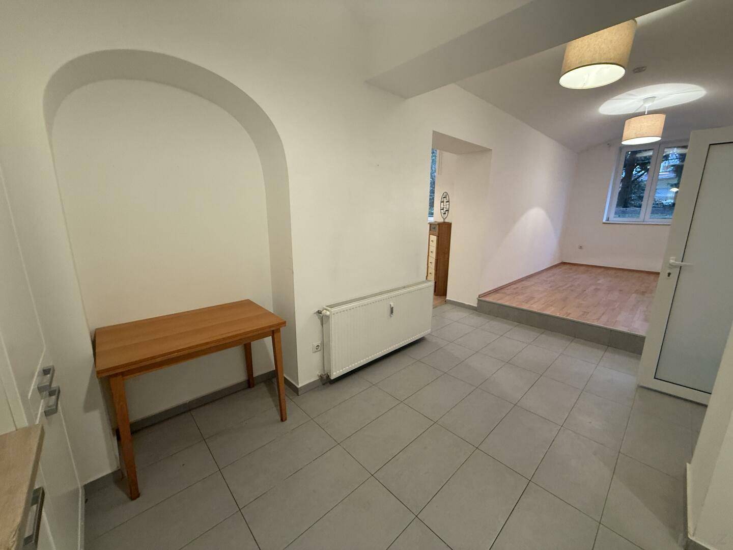 Offener Wohnbereich mit Fliesenboden und Übergang zu einem erhöhten Zimmer mit Parkett.