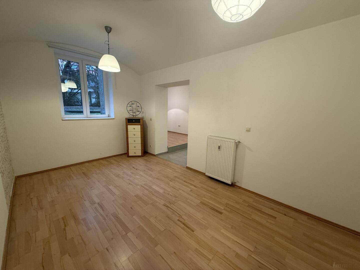 Wohnzimmer mit Parkettboden, Fenster und Blick in den angrenzenden Bereich, gut beleuchtet.