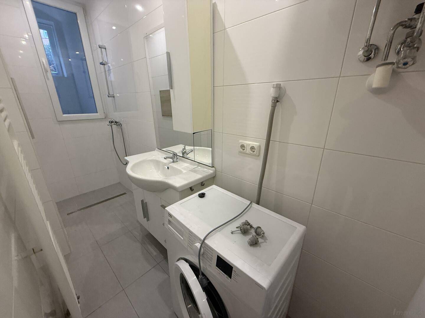 Modernes Badezimmer mit Waschbecken, Waschmaschine und Handtuchheizkörper, hell gefliest.