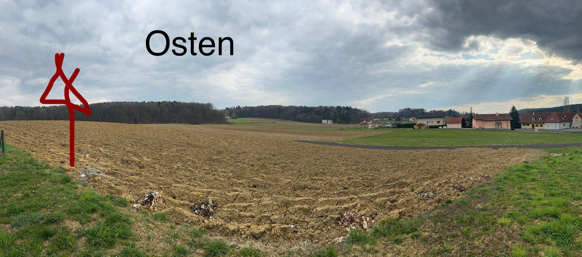 Blick nach Osten über ein weites Feld mit ländlicher Bebauung am Horizont unter bewölktem Himmel.