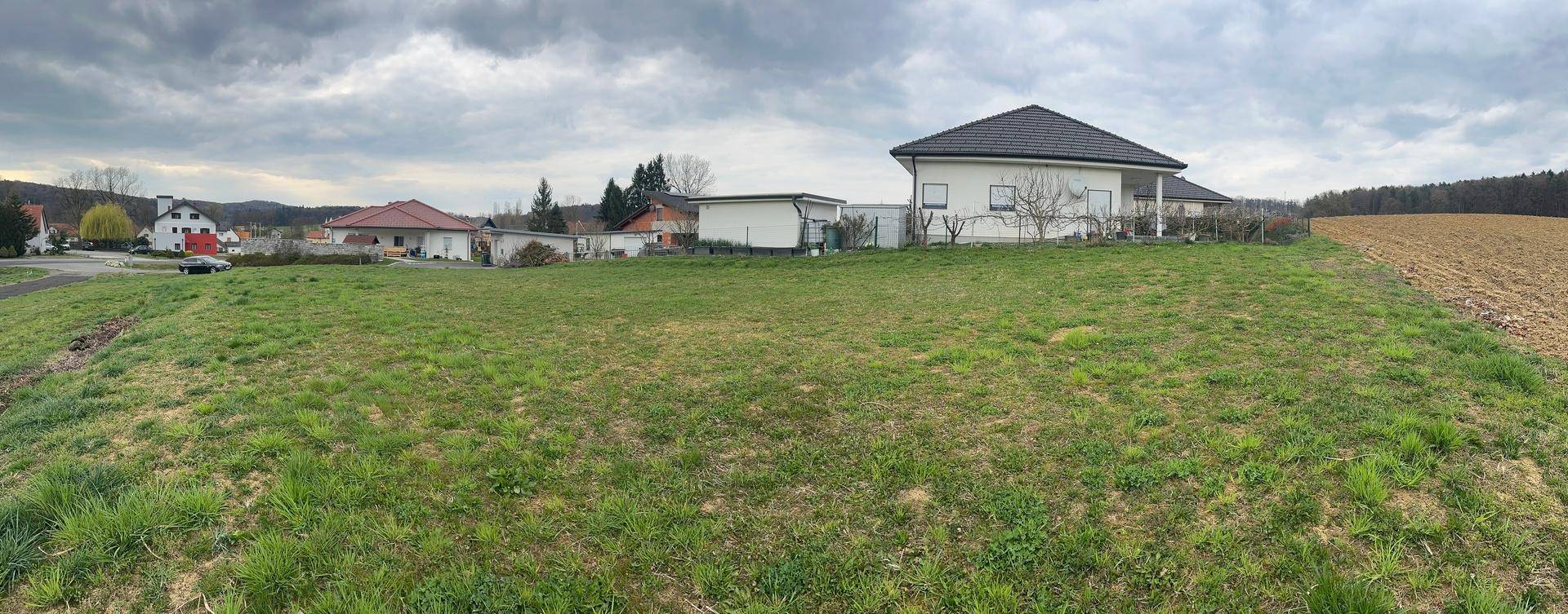 Großes Grundstück mit Rasenfläche und einem modernen Haus im Hintergrund, umgeben von Natur.