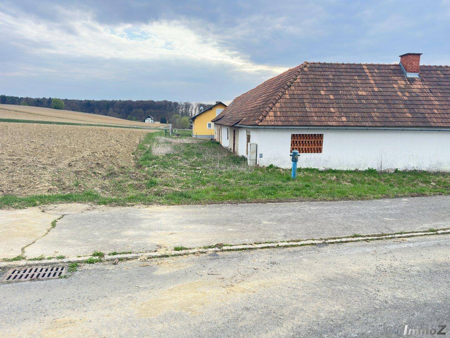 Seitenansicht eines Gebäudes mit Ziegeldach und angrenzendem Feld unter bewölktem Himmel.