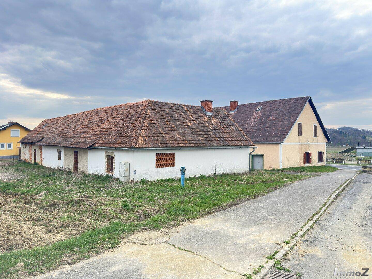 Mehrere ländliche Gebäude mit Ziegeldächern und einem gepflasterten Weg unter bewölktem Himmel.