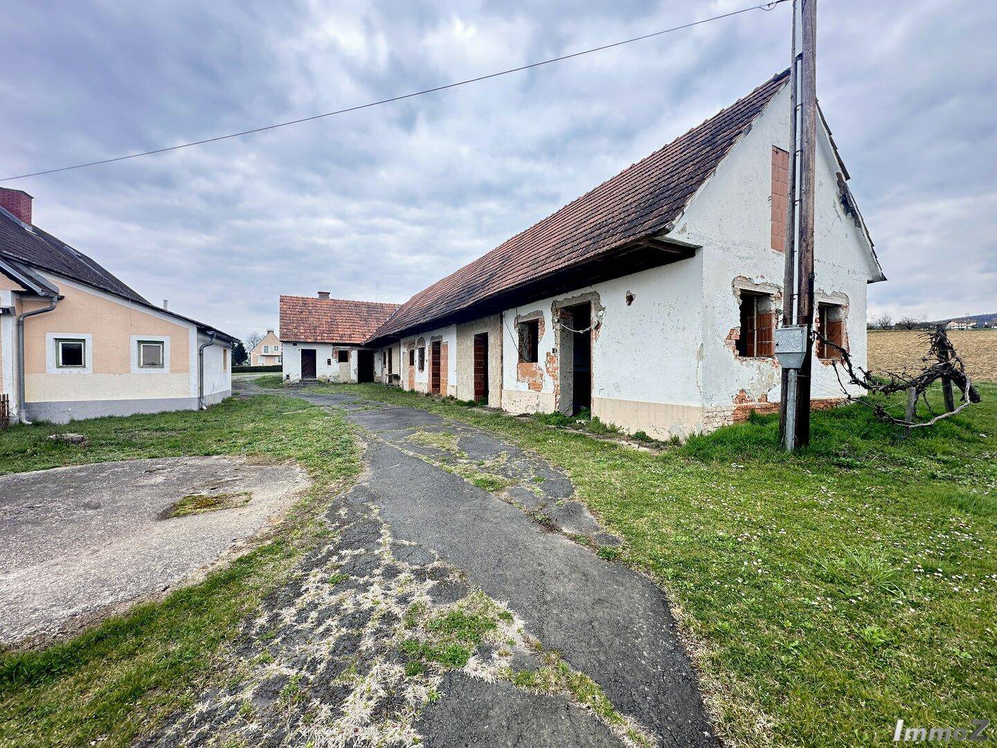 Altes, renovierungsbedürftiges Gebäude mit bröckelndem Putz und einem langen Zufahrtsweg in ländlicher Umgebung.