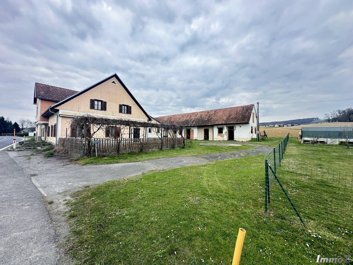 Mehrere Gebäude mit Satteldächern und weitläufigen Grünflächen in ländlicher Umgebung unter bewölktem Himmel.