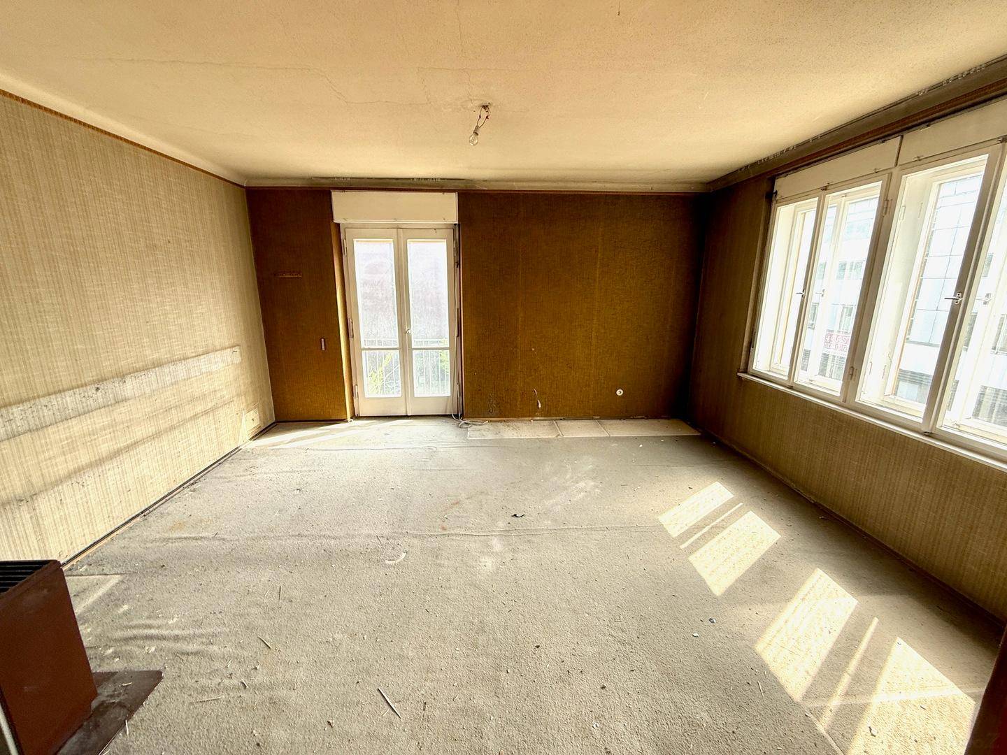 Geräumiger Wohnbereich mit Teppichresten, Balkonzugang und viel natürlichem Licht.