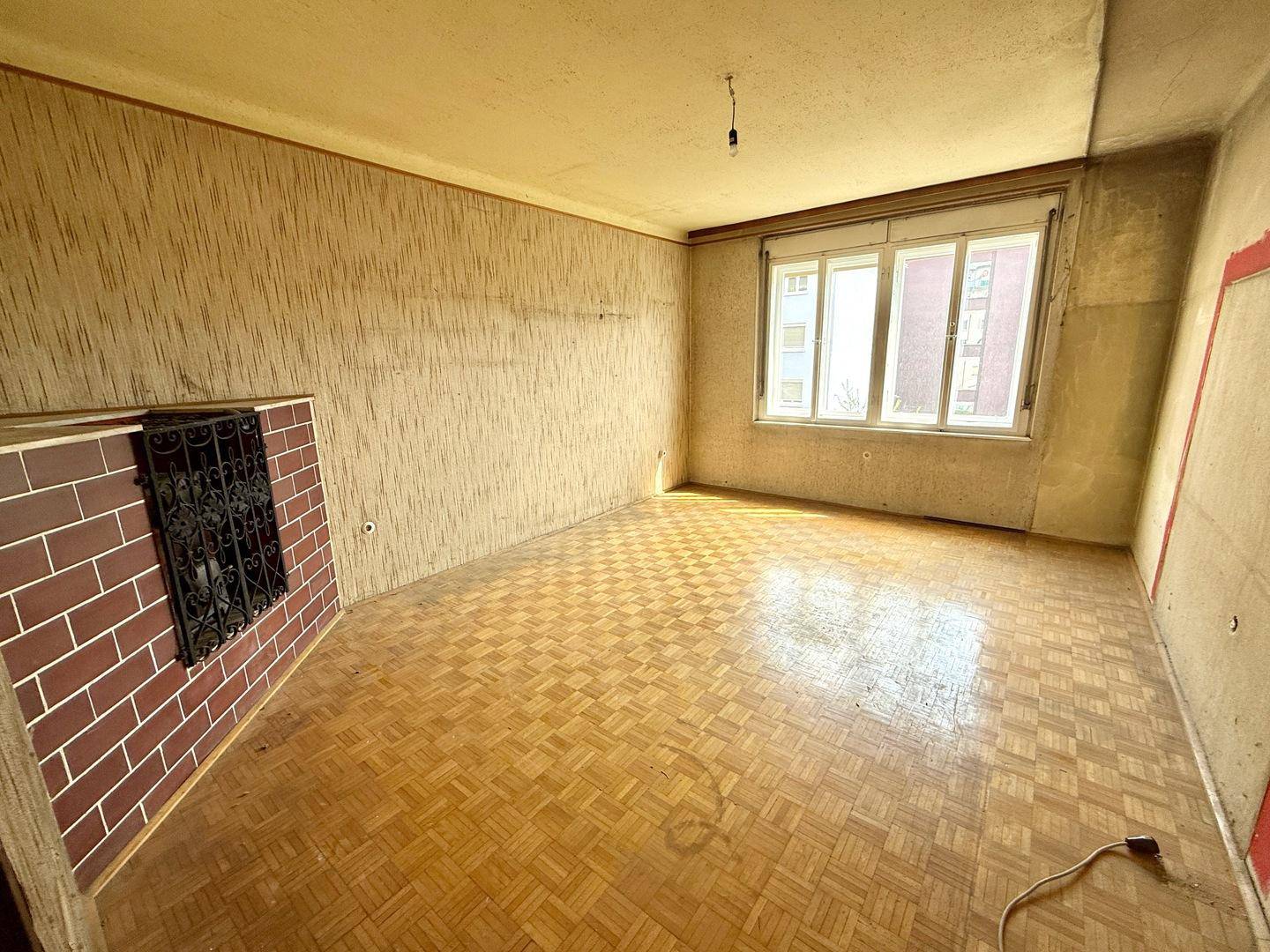Wohnzimmer mit Parkettboden, strukturierten Tapeten und einem gemauerten Kamin, ideal für Renovierung.