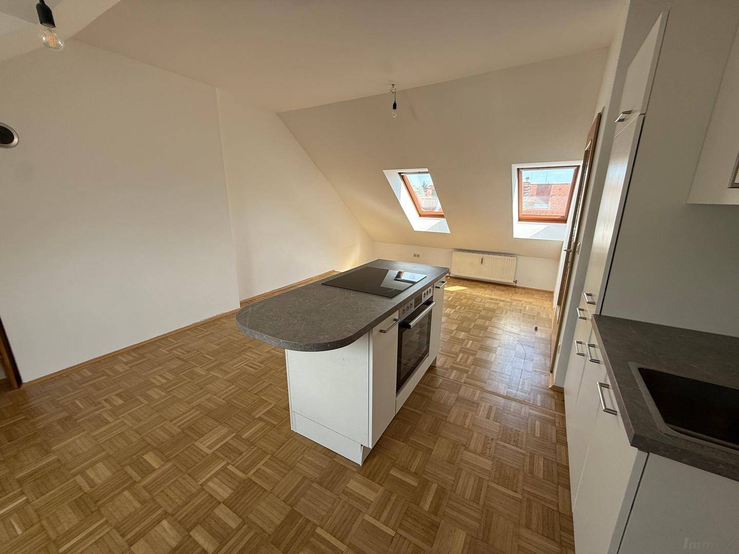 Moderne Kücheninsel mit Induktionskochfeld und Backofen, umgeben von hellem Parkettboden und Dachfenstern.