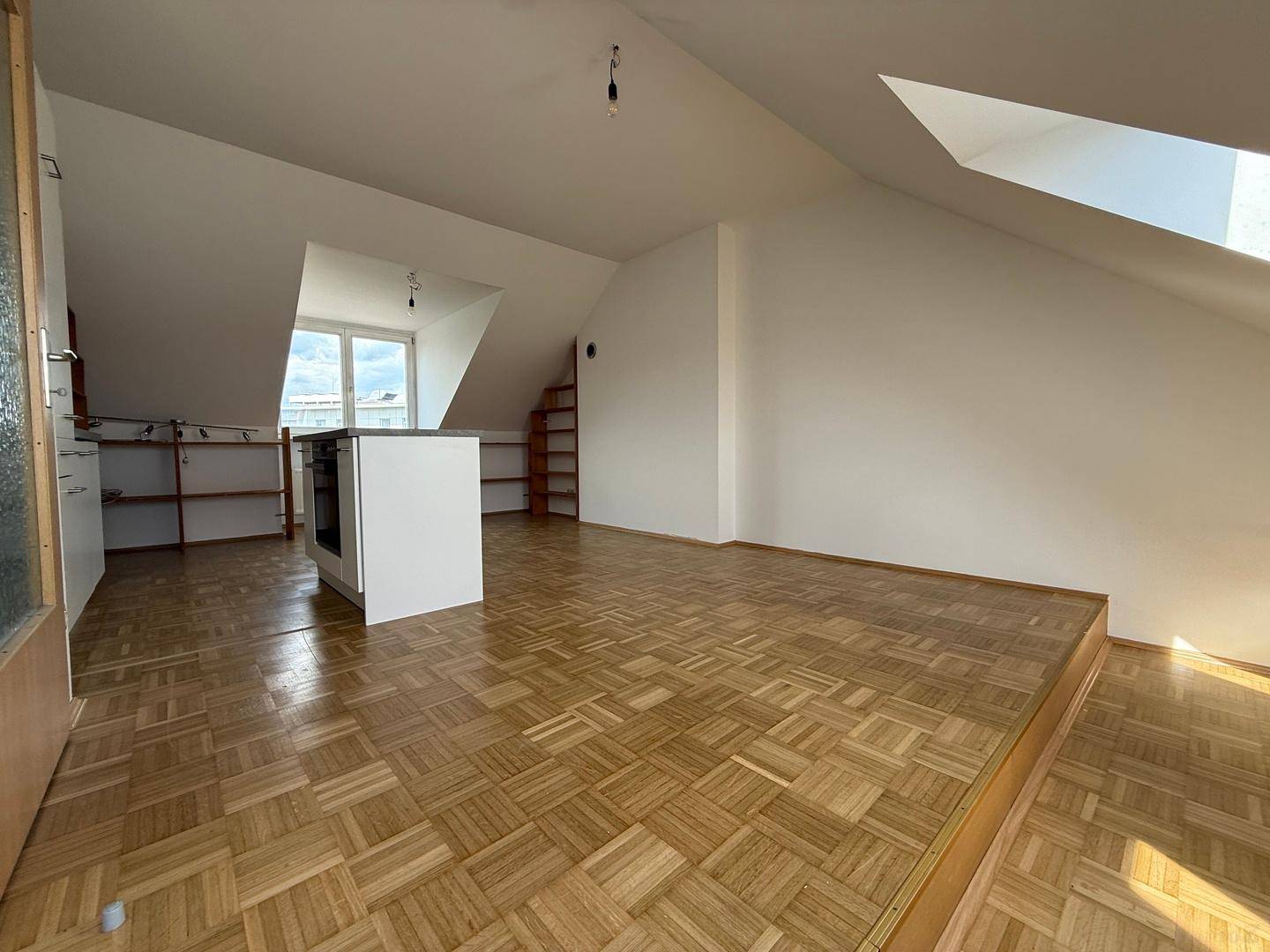 Weitläufiger offener Wohnbereich mit Parkettboden, erhöhter Fläche und Blick auf die Küchenzeile.