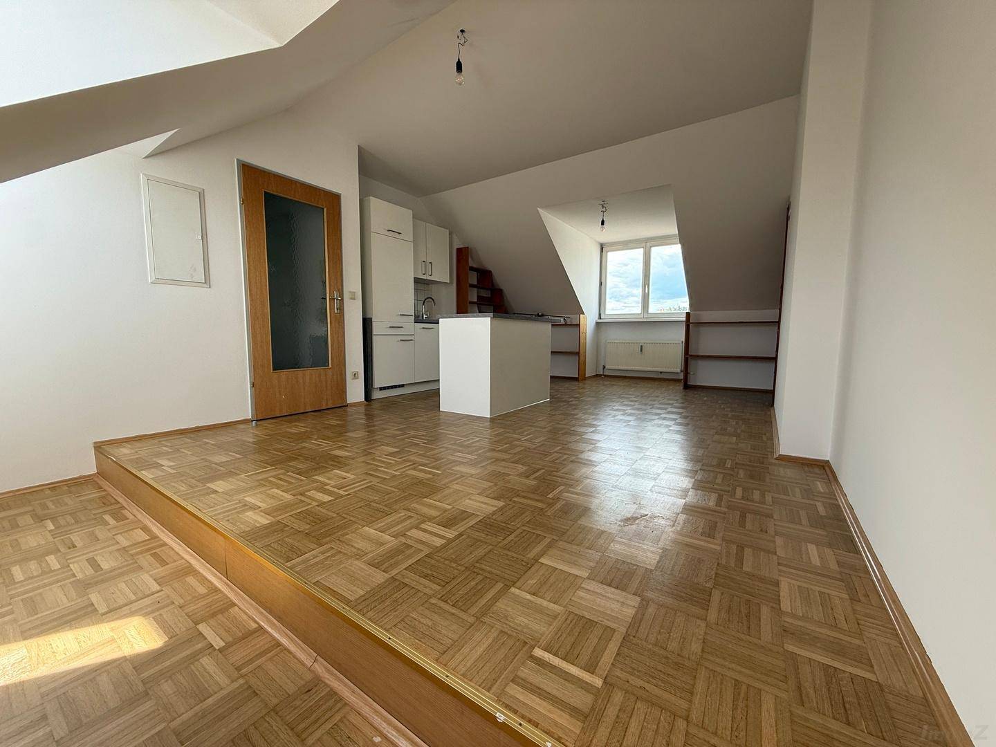 Offener Wohnbereich mit Parkettboden und einer erhöhten Plattform, die den Raum strukturiert.