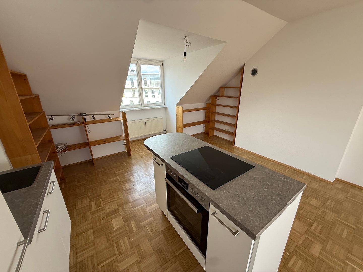 Offener Wohnbereich mit Kücheninsel, integriertem Backofen und Parkettboden unter Dachschrägen.