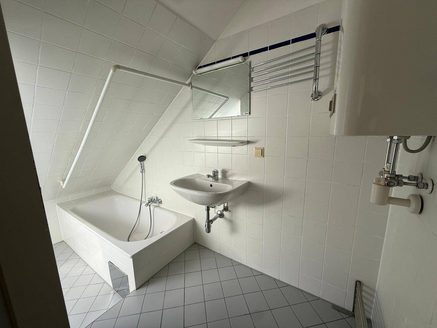 Badezimmer mit Badewanne, Waschbecken und Dachschräge, ausgestattet mit weißen Fliesen.