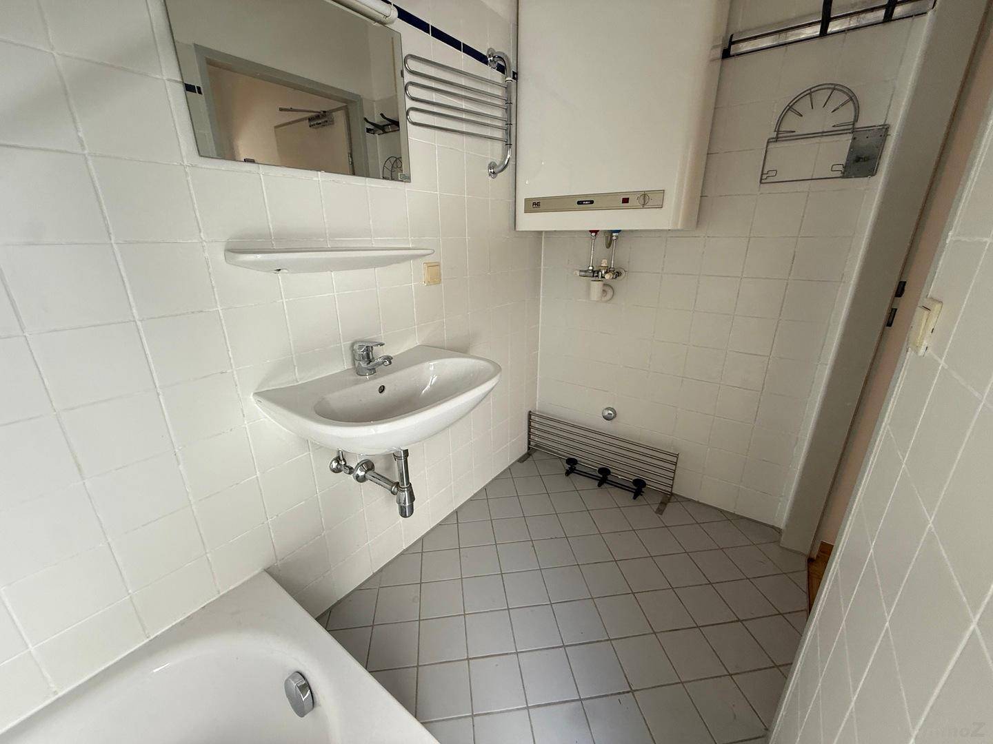 Detailansicht des Badezimmers mit Waschbecken, Spiegel und Handtuchheizkörper, alles in hellen Fliesen.