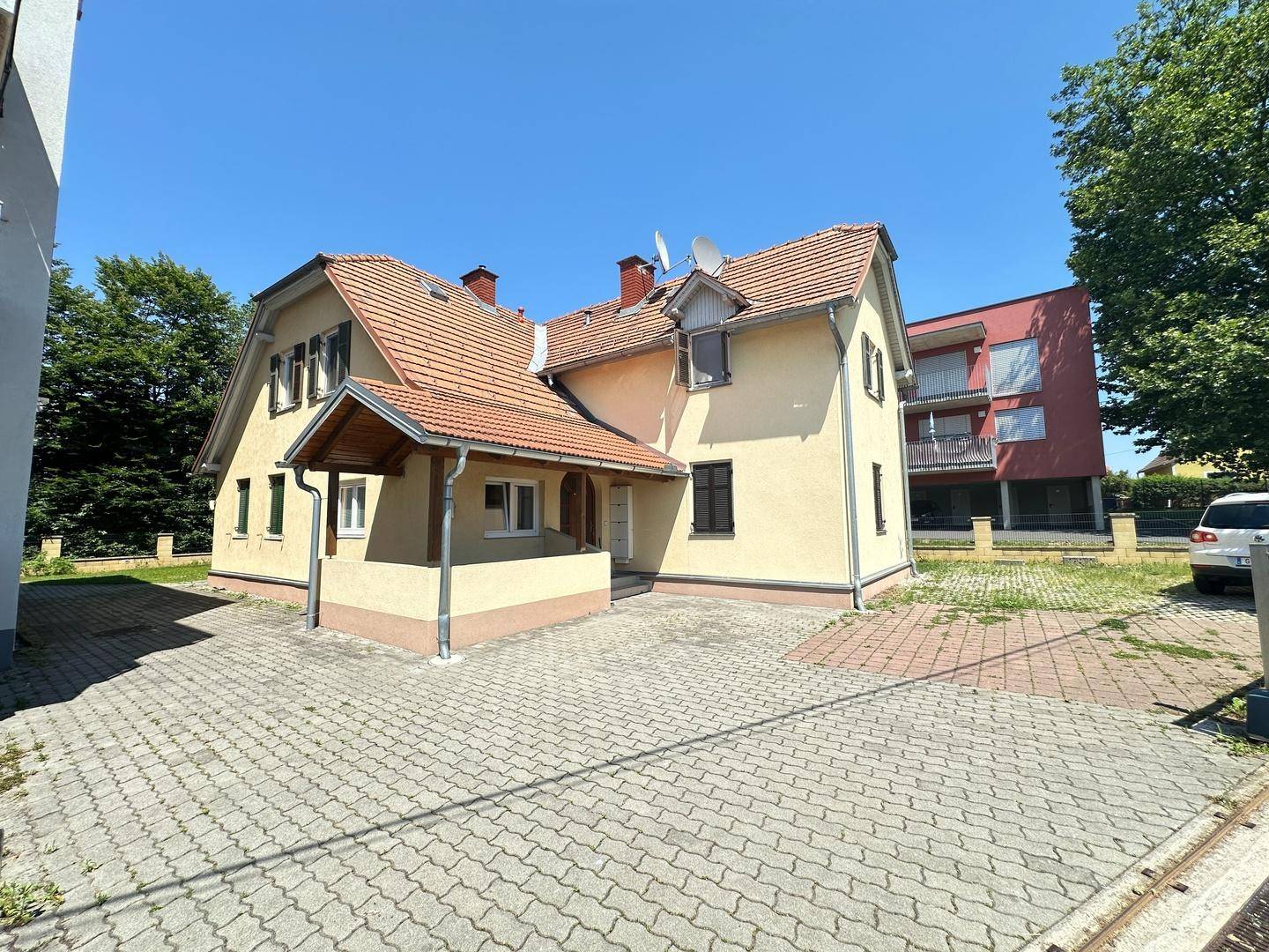 Traditionelles Haus mit überdachtem Eingangsbereich und gepflasterter Fläche vor dem Gebäude.