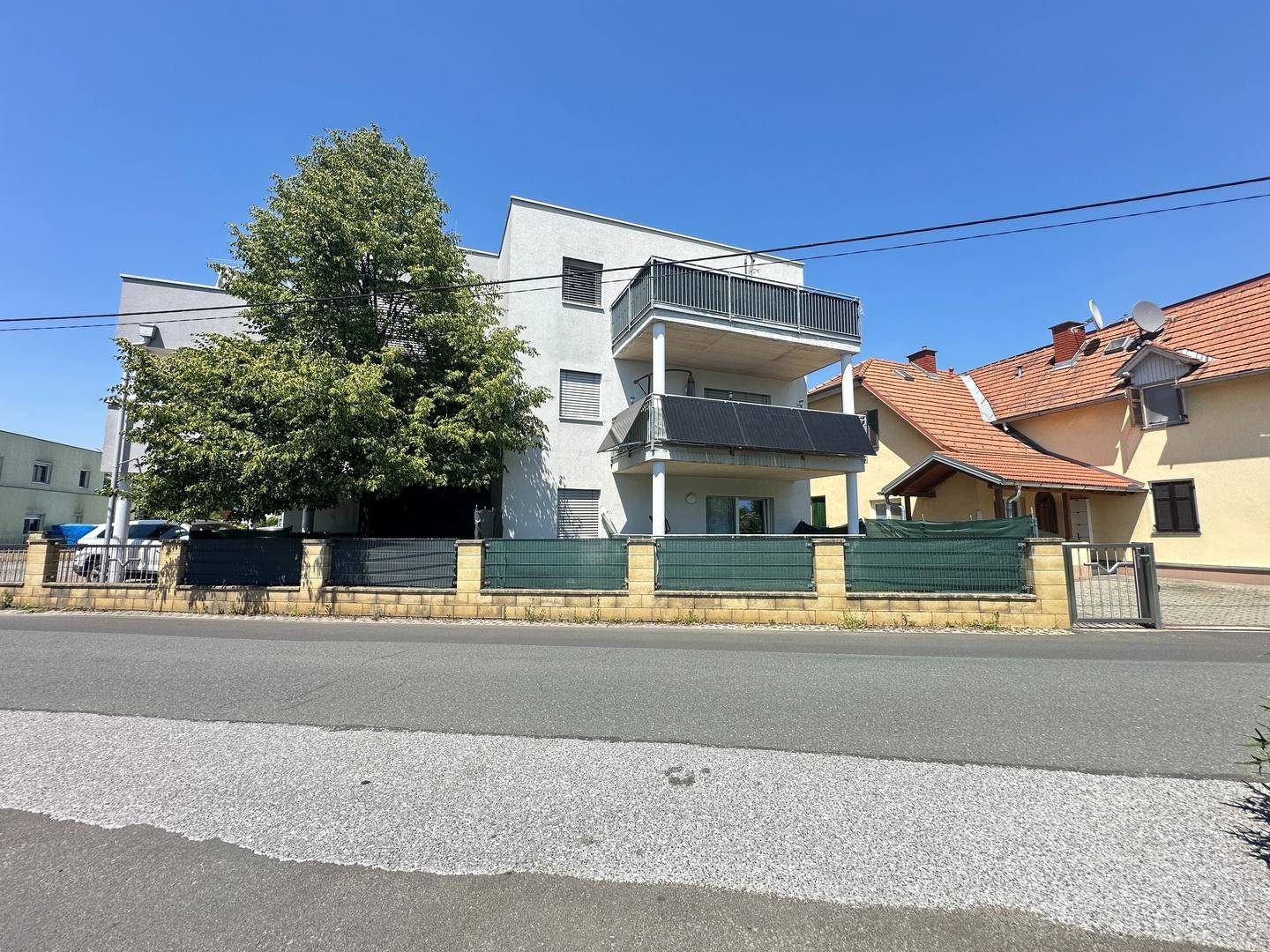 Moderne Gebäudefassade von der Straße aus gesehen mit Balkonen und Solarpaneelen.