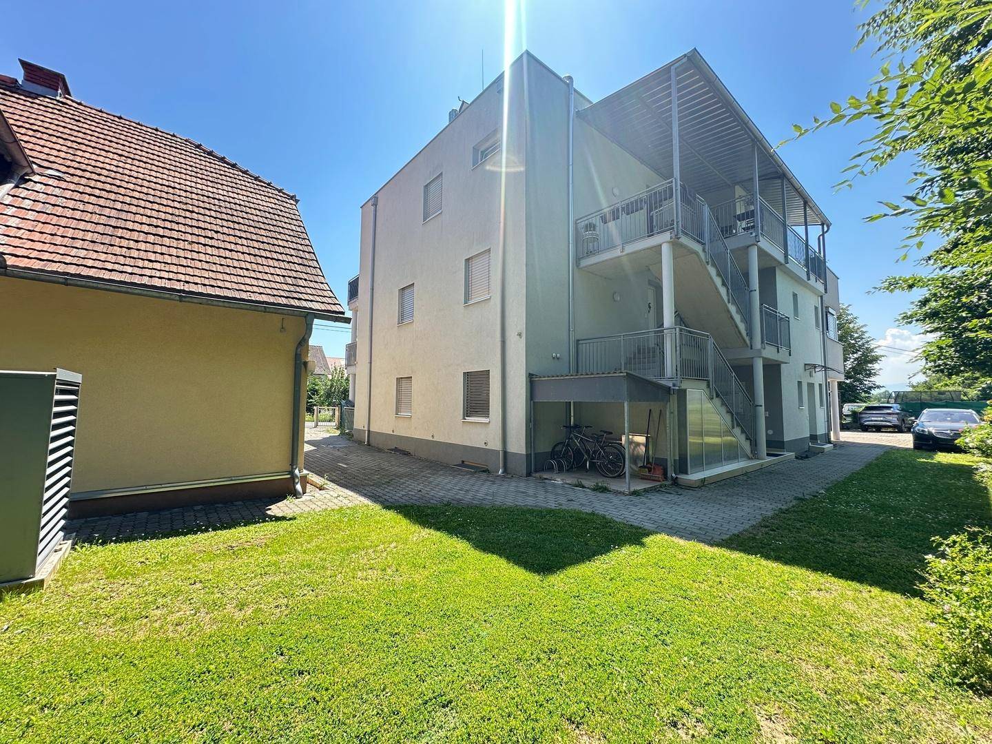Rückseite des modernen Gebäudes mit Außentreppen und Fahrradabstellplatz, neben dem traditionellen Haus.