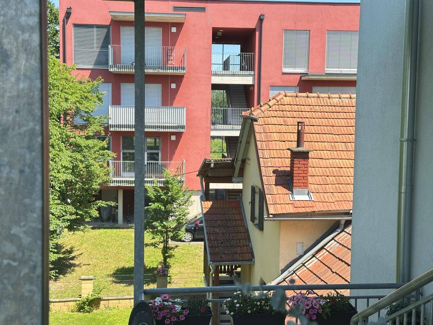 Nahaufnahme vom Balkon mit Blick auf das rote Gebäude und das Ziegeldach des Nachbarhauses.