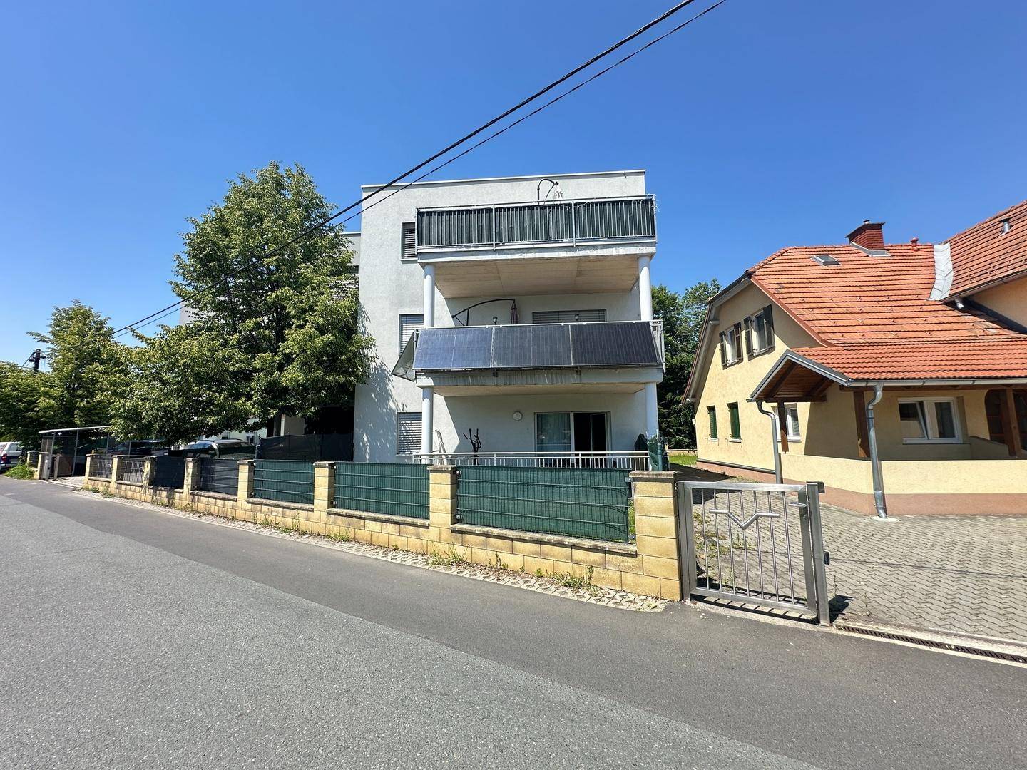 Ansicht des modernen Gebäudes von der Straße mit Balkonen, Solarpaneelen und einem Eingangstor.