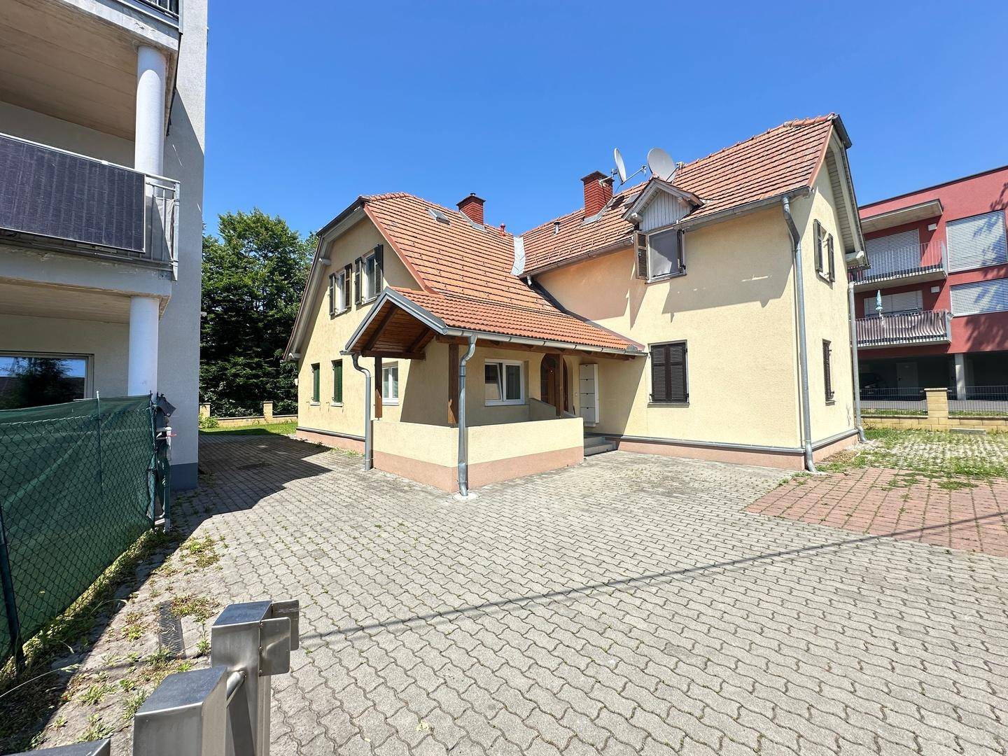 Traditionelles Haus mit Ziegeldach und gepflasterter Einfahrt, umgeben von Grünflächen.