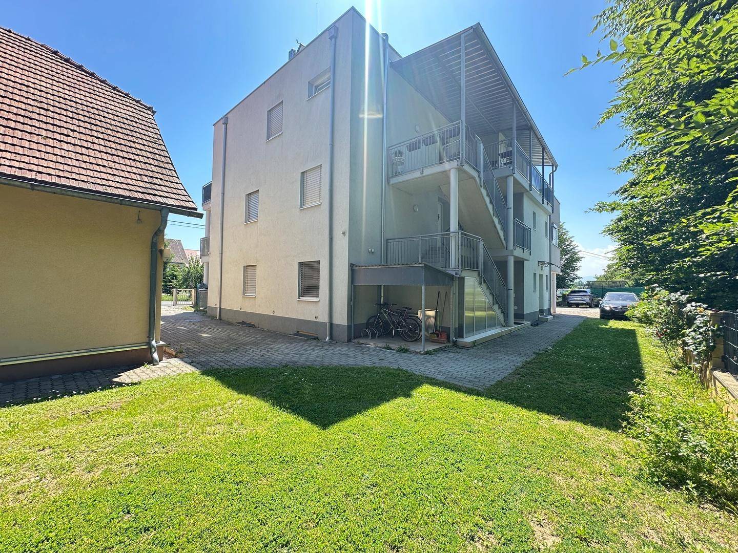 Rückseite des modernen Gebäudes mit Außentreppen und Fahrradabstellplatz, neben dem traditionellen Haus.
