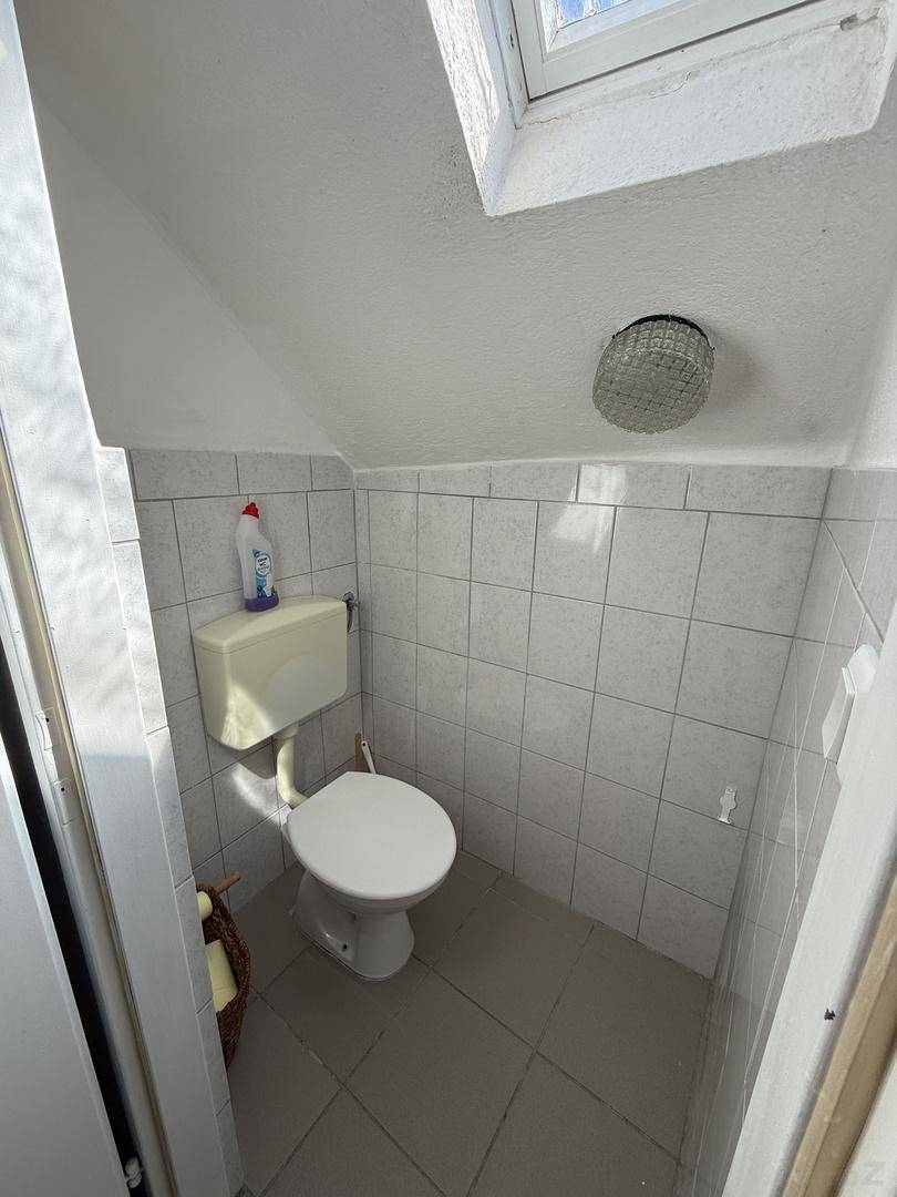 Kleines Gäste-WC mit Dachfenster, hellen Fliesen und einfacher Ausstattung.