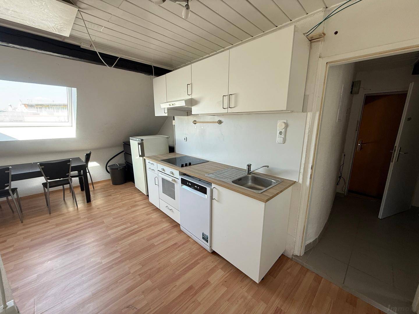 Funktionale Küche mit weißen Schränken, Spülmaschine und Essbereich unter dem Dachfenster.