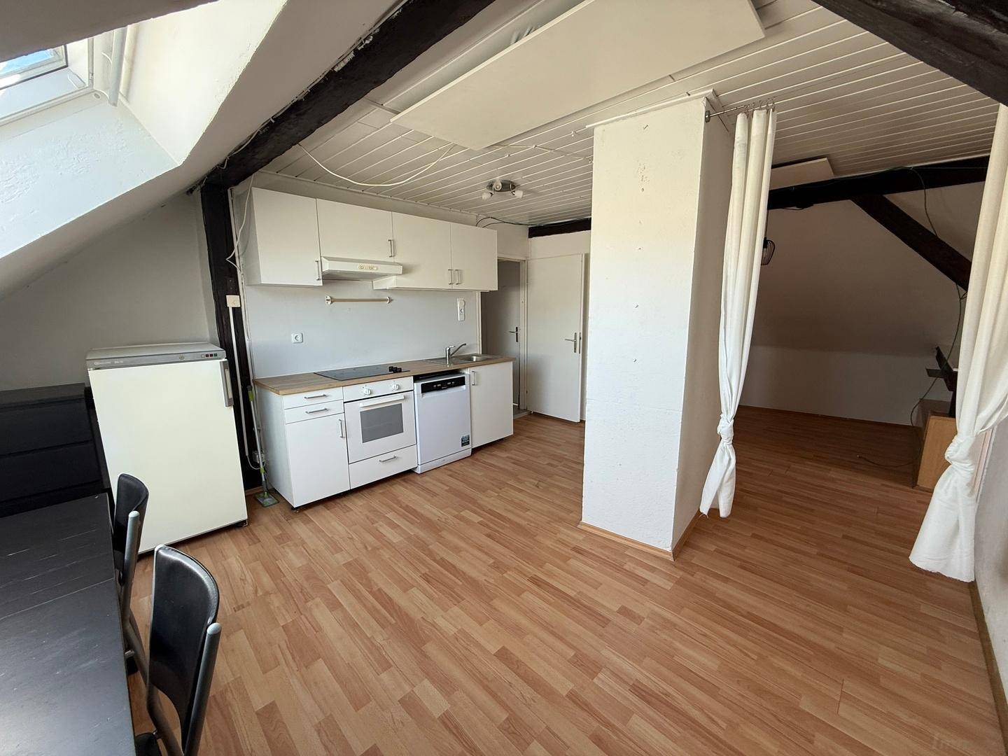 Offene Küche mit weißen Schränken und Essbereich in einer Dachgeschosswohnung mit Holzbalken.