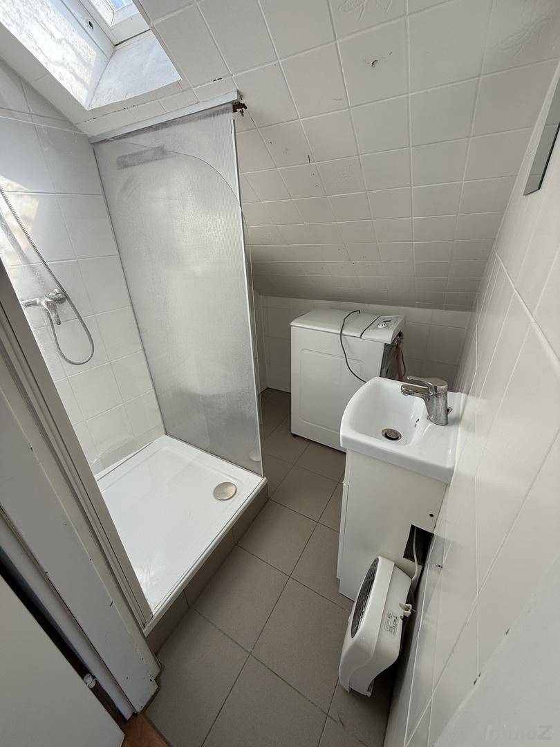 Kleines Badezimmer mit Dusche, Waschbecken und Waschmaschine unter der Dachschräge.