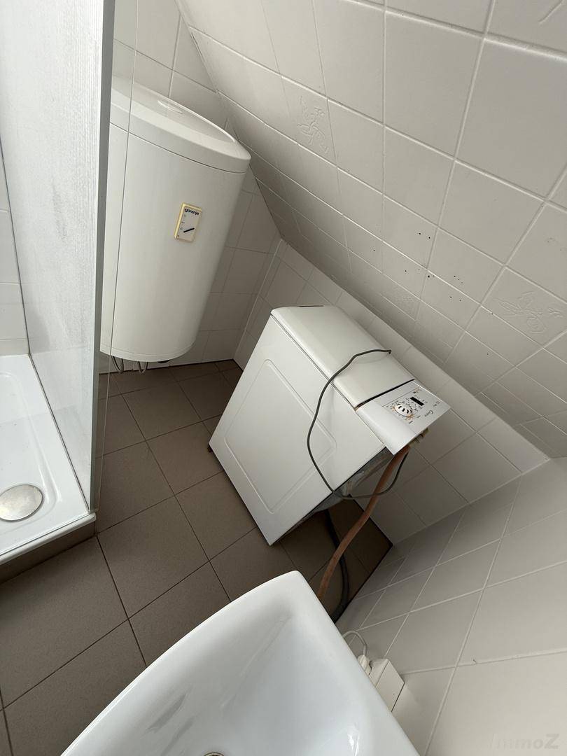 Badezimmer mit Waschmaschine, Warmwasserboiler und Duschbereich unter der Dachschräge.