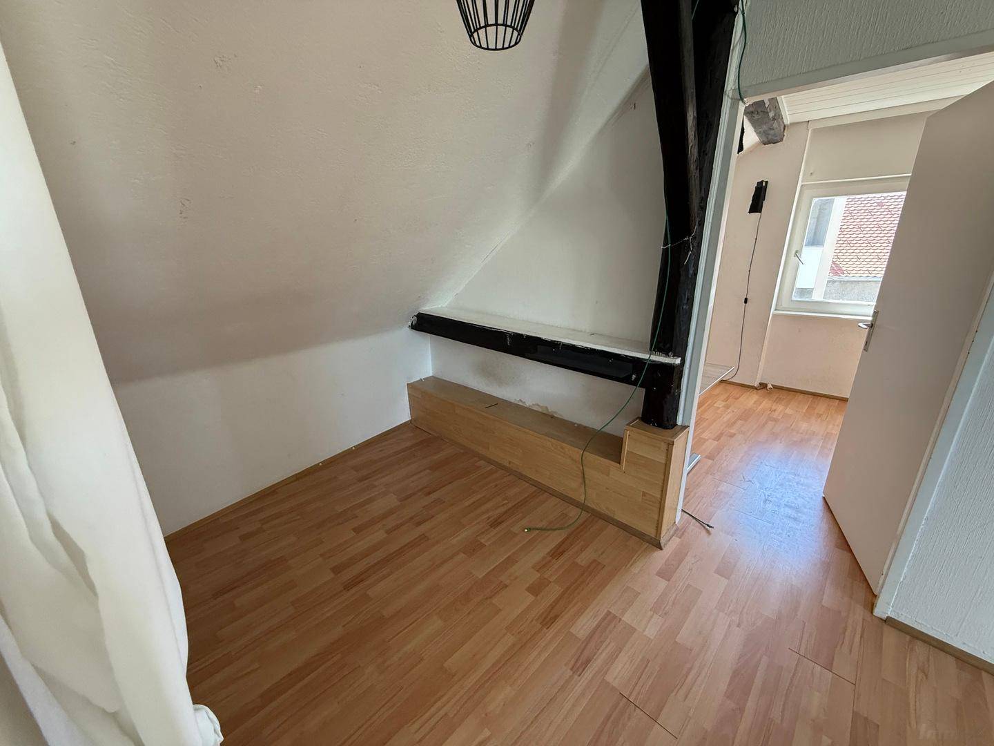 Leeres Zimmer im Dachgeschoss mit Holzbalken, Dachschräge und Laminatboden.