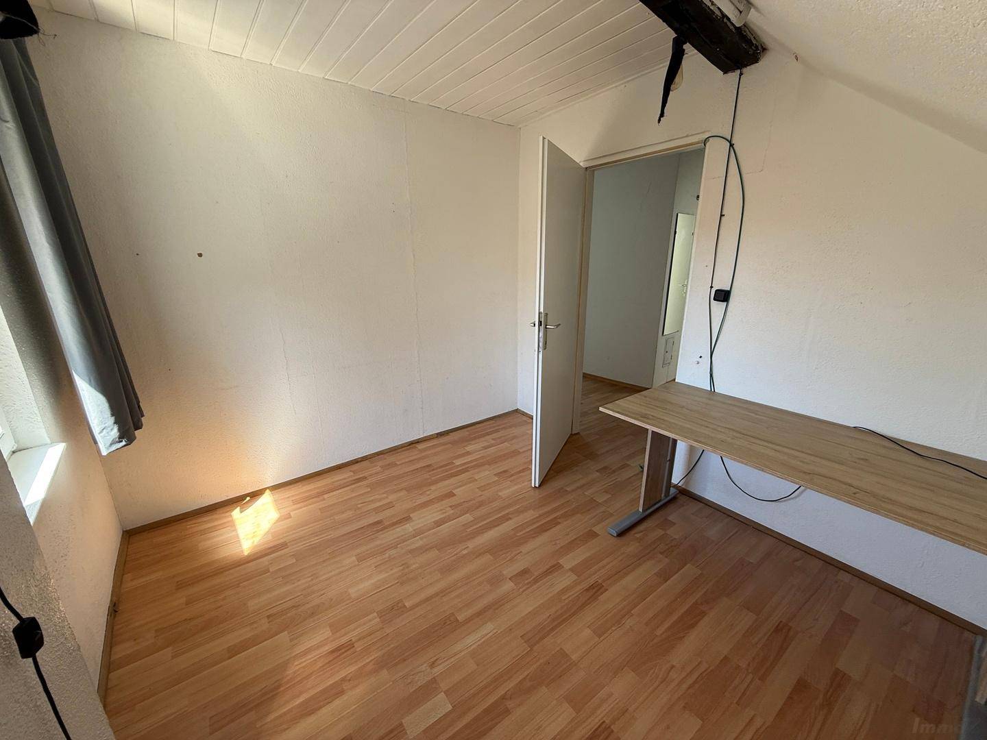 Helles Zimmer mit Laminatboden und Zugang zu einem weiteren Raum, geeignet als Schlaf- oder Arbeitszimmer.